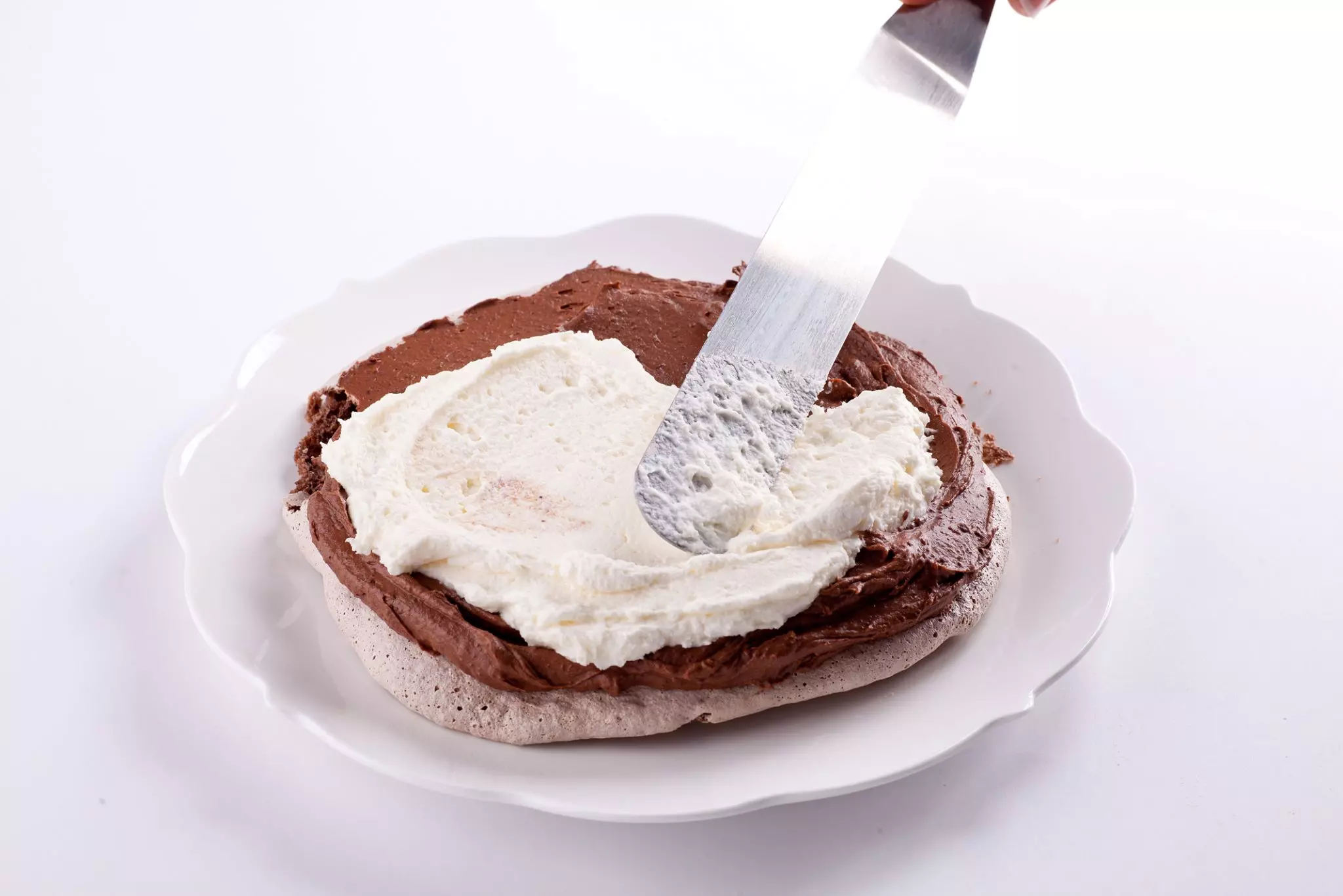 הרכבת העוגה: מניחים עיגול מרנג בצלחת הגשה, מורחים מעליו קרם שוקולד מריר ומעליו קרם שוקולד לבן.