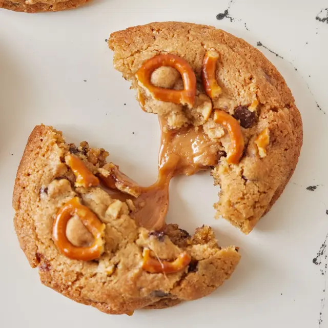 עוגיות שוקולד צ’יפס מטריפות עם שברי בייגלה פריך מעל והפתעת קרמל מלוח שמתגלה רק בביס הראשון - לא תאמינו כמה קל להכין אותן!
איך מכינים? 
מצרכים:
מצרכים
200 גרם חמאה
200 גרם (1 כוס) סוכר לבן
50 גרם (1/4 כוס) סוכר חום כהה
1 ביצה L
280 גרם (2 כוסות) קמח לבן
1 כפית סודה לשתייה
200 גרם שוקולד פרה מריר קצוץ
20 סוכריות טופי קרמל
חופן בייגלה מלוח

אופן ההכנה:
- ממיסים את החמאה (זהירות לא להרתיח אותה אלא רק עד לנקודת המסה) בקערה ומוסיפים את 2 סוגי הסוכר. טורפים היטב.
- מוסיפים ביצה וטורפים.
- מוסיפים קמח וסודה לשתייה ומערבבים עד שהקמח נטמע.
- מוסיפים שוקולד קצוץ ומערבבים.
- יוצרים כדורים בגודל פינג פונג ומשטחים על היד. מניחים באמצע סוכריית קרמל (אפשר גם 2) וסוגרים לצורת כדור מעט פחוס.
- מטביעים בחלק העליון בייגלה ומעבירים את העוגיות הממולאות למקרר לשעה או עד יומיים.
- מניחים את העוגיות על תבנית תנור עם נייר אפייה, מקפידים להשאיר רווח בינהן, ואופים בתנור שחומם מראש ל-190 מעלות ואופים 12-15 דקות.
- מצננים מעט ואוכלים בהנאה.