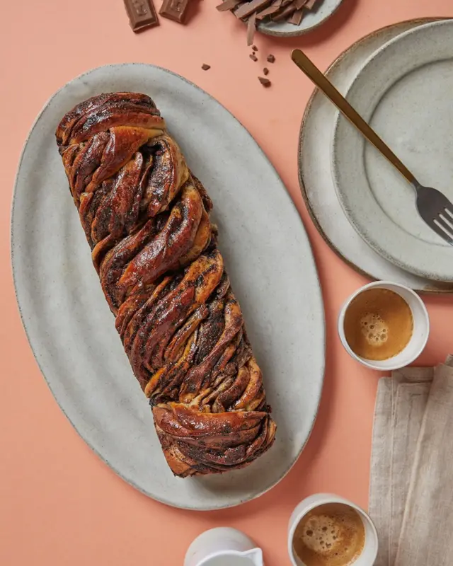 שבת חורפית וריח של עוגת שמרים מפוצצת שוקולד בבית, הבצק שלה רך וחמאתי, היא משובצת בקוביות שוקולד פרה, ותישאר טעימה גם יום ויומיים אחרי האפיה, אבל לא בטוח שיישאר משהו💕
איך מכינים? 
לבצק:
500 גרם קמח לבן
1 כף שמרים יבשים או 3 כפות שמרים טריים
1/2 כוס סוכר לבן
1 מיכל שמנת מתוקה או כוס חלב או כוס מים
2 ביצים L
100 גרם חמאה מומסת
למילוי:
50 גרם חמאה מומסת
1/2 כוס שמן
180 גרם סוכר חום בהיר
5 כפות קקאו
200 גרם שוקולד פרה מריר או חלב עלית

לסירופ:
3/4 כוס מים
1/2 כוס סוכר

אופן ההכנה: 
- בקערת מיקסר עם וו לישה מניחים את כל מצרכי הבצק פרט לחמאה. מערבלים במשך דקה.
- מוסיפים את החמאה ומערבלים במשך 8-10 דקות.
- מכסים במגבת ומאפשרים לבצק לנוח במשך 45 דקות (אם מאוד קר בחוץ אפשר גם שעה ורבע). הבצק אמור לתפוח אבל לא להכפיל את נפחו אלא יותר כמו 3/4 התפחה.
- מכינים את המילוי: ממיסים את החמאה במיקרו בתוך קערה.
- מוסיפים את שאר מצרכי המילוי חוץ מהשוקולד, לפי הסדר ברשימה, ומערבבים היטב עד שנוצר ממרח די אחיד (זה בסדר אם ישנם גרגירי סוכר).
- מחלקים את הבצק ל-2 ומרדדים למלבן דק. כמה דק? ככל שהבצק יהיה דק יותר ככה יהיה בו פחות בצק ויותר מילוי, שזה האידיאל. איזה גודל מלבן? ככל שהמלבן יהיה רחב יותר ככה בגלגול שלו לרולדה יהיו יותר שכבות ולכן בכל ביס יהיה יותר שוקולד.
- מורחים שכבה נדיבה של מילוי על הבצק, מקפידים למרוח ממש עד סוף הבצק, ומפזרים שוקולד קצוץ.
- מגלגלים לרולדה ארוכה, חותכים את הרולדה לאורכה ומסובבים את 2 החצאים אחד עם השני עד ליצירת בורג. מניחים את העוגה בתבנית אינגליש קייק משומנת עם נייר אפייה כשהשוקולד פונה כלפי מעלה.
- מכסים את העוגות במגבת ומתפיחים במשך 35 דקות.
- בינתיים מחממים תנור ל-190 מעלות.
- מברישים את העוגות בביצה טרופה ואופים במשך 40 דקות או עד שהעוגות זהובות. חשוב לבדוק אותן כבר אחרי חצי שעה – תלוי באיזה גודל הכנתם את העוגות, מה עובי הבצק וכדומה.
- 10 דקות לפני שהעוגות מוכנות, מחממים בסיר קטן את המים והסוכר עד שהסוכר נמס לגמרי. ברגע שהעוגות יוצאות מהתנור מברישים אותן, בנדיבות רבה (לא לפחד, הסירופ נספג ויותיר את העוגה רכה כמה ימים), בסירופ הסוכר.